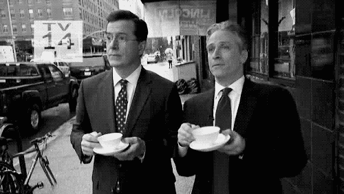 Two white men in suits, Stephen Colbert and Jon Stewart, say "Wow! Bravo!" while sipping from teacups and holding saucers